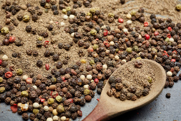 Wooden spoon full of allspice seeds and grind black pepper on the mixture of peppers background,...