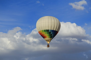 Many colored aerostatic balloon flying in a blue sky with white clouds
