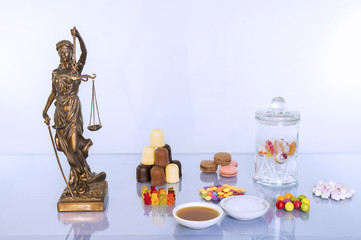Justitia Statue steht auf dem Tisch mit vielen süßen Lebensmitteln. Zum Vergleich stehen dort ...