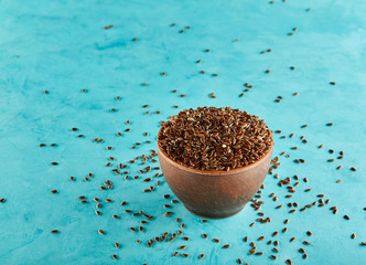 Flax seeds in a clay bowl isolated on blue background, close-up