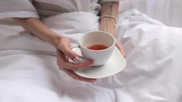 female hands holding a mug with tea in bed