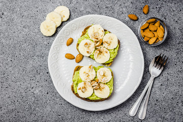 Toasts with caramelized bananas, avocado and nuts on concrete background. Top view, space for text. 