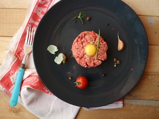 Tartar raw fresh minced meat with quail egg, cherry tomatoes, garlic and pepper mix. Gourmet eating. Closeup.