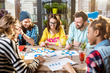 Group of caucasian coworkers dressed casually working together with documents and laptops at the big table in the beautiful cafe interior