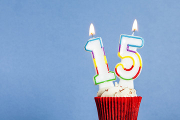 Number 15 birthday candle in a cupcake against a blue background