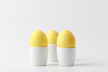 Three yellow painted easter eggs in egg stands on white