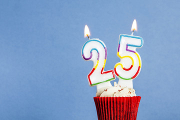 Number 25 birthday candle in a cupcake against a blue background