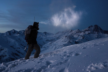 Extreme tourism. Brave expeditor lights the way with a headlamp at night winter mountains. Man with...