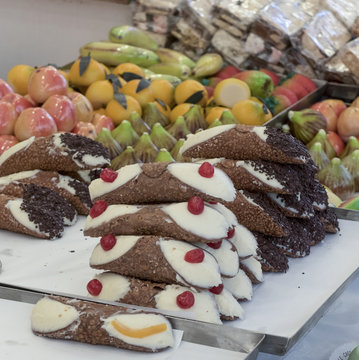steel tray containing typical Sicilian sweets. In the foreground the famous Sicilian cannoli stuffed with ricotta and decorated with candied cherries and chocolate chips. Fruit-shaped marzipan sweets.