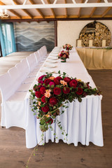 Banquet table decorated with red dahlias and another flowers. White plates are standing on the table. Wedding