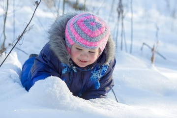 Fototapeta na wymiar Little baby girl play with snow on bright sunny winter day