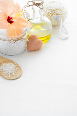 Fototapeta na wymiar Wellness setting. Sea salt in glass, soap, towel, olive oil and flowers on white textured background. Space for copy. Flat lay