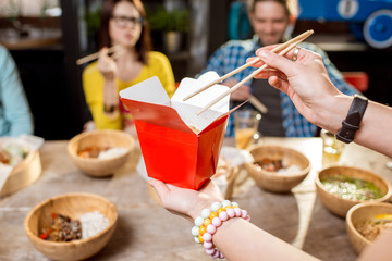 Holding a box with asian food indoors with table full of food on the background
