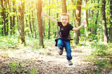 Happy blond boy jumping in sunny day on nature.