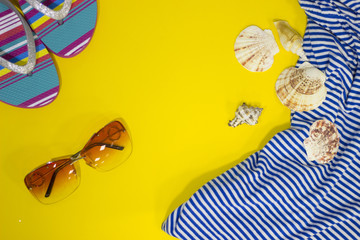 Travel and tourism concept. A bright yellow background with sunglasses, a striped shirt and slippers, top view. Space for a text or product display.