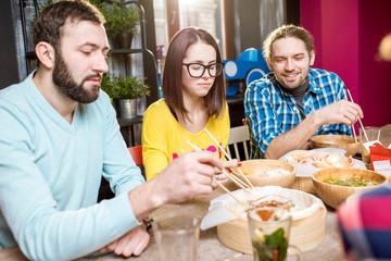 Young friends having fun during the dinner with asian food sitting at the modern restaurant