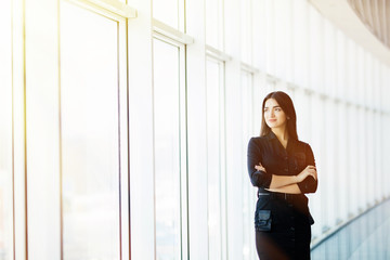 Businesswoman crossed hands portrait in office with panormic windows.