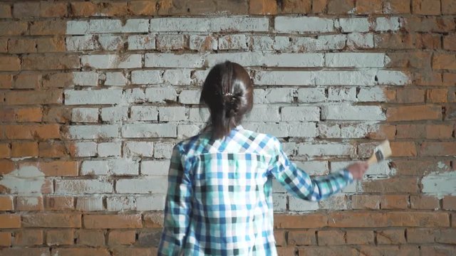 The girl whitens brick wall. Hipster girl whitewash the walls at home. Holds in the hands of a brush with paint.