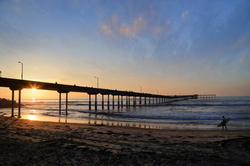 Fototapeta na wymiar A surfer walks on Ocean Beach near the pier in San Diego, California.