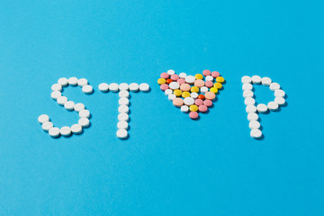 Medication white, colorful round tablets in word Stop isolated on blue background. Pills heart shape, form, letter. Concept of health, treatment choice healthy lifestyle. Copy space advertisement.