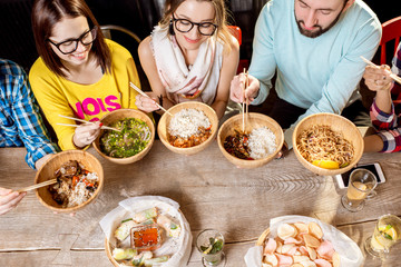 Friends eating asian food sitting at the wooden table