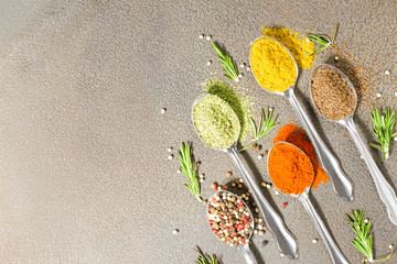 Various spices in a spoon on grey background