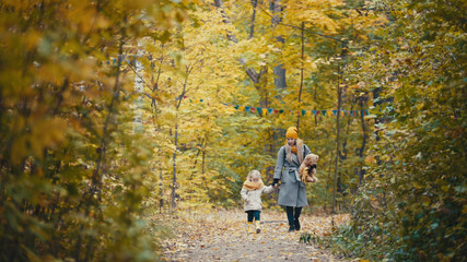 Fototapeta premium Pretty blonde little daughter with her mommy walks in autumn park - have funny and collect leaves