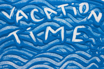 Vacation time inscription on a blue colored sand with waves, top view, flat lay