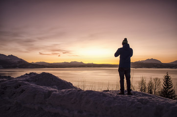 Fototapeta na wymiar Silhouette of Person by Lake and Snow Covered Landscape at Sunset