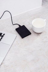 External hard drive connected to the laptop and white mug on grey concrete background. File storage, back up, info recovery concept. Flat lay, copyspace for text.