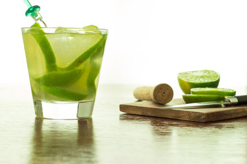 A glass of Caipirinha, is the most famous brazilian drink - lemon cachaca and ice - wood board - slice of lemon - knife on a wood table - front foto