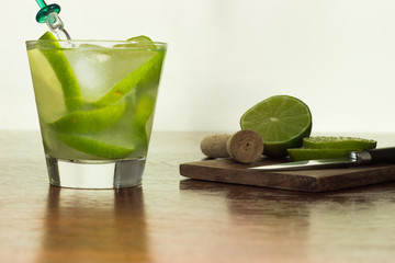 A glass of Caipirinha, is the most famous brazilian drink - lemon cachaca and ice - wood board - slice of lemon - knife on a wood table - front foto