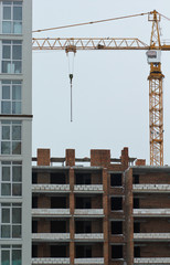 Yellow construction tower crane in action and unfinished brick multistory building next to finished modern house