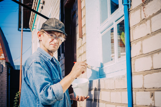 Mature Man In Glasses, Painting Window Frame Outside Of Private 