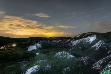 Night landscape with chalk ridges under cloudy and starry sky. White cretaceous hills at night. Natural archaeological monument - Krapivenskoye ancient settlement, Belgorod region, Russia.