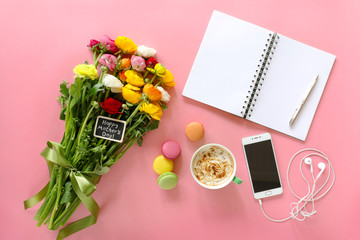 Happy Mother's Day note on the buttercup flowers, cup of cappuccino, makarons cake, mobile with headphones, notebook, pen on the pink background, Happy Mother's Day concept.