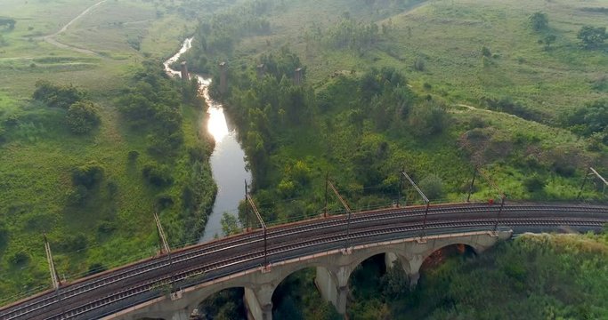 Flying into the sun above picturesque seven arch rail bridge straddling river aerial 4K