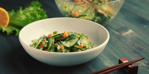 Chinese cucumber salad on the white plate. Chopsticks. Asian cuisine. Bell pepper, cucumber and sesame seeds. Vegetarian dish. Wide photo.