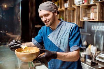 Portrait of caucasian chief cook in uniform decorating meal in the wooden plate at the asian restaurant kitchen