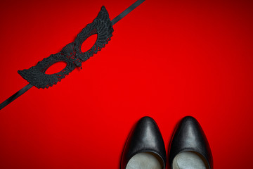 Top view of a sexy black mask and high heels on a red intense background