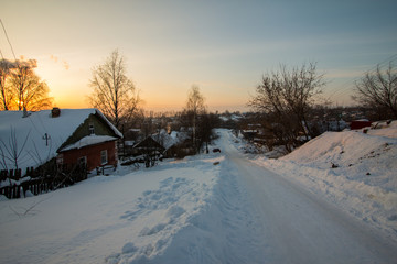 Snow-covered rural street lit by the setting sun