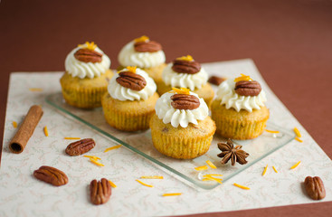 Cupcakes decorated with pecan nuts, orange zest and spice on brown background