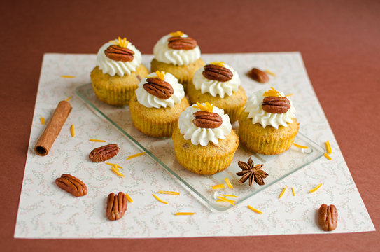 Cupcakes decorated with pecan nuts, orange zest and spice on brown background