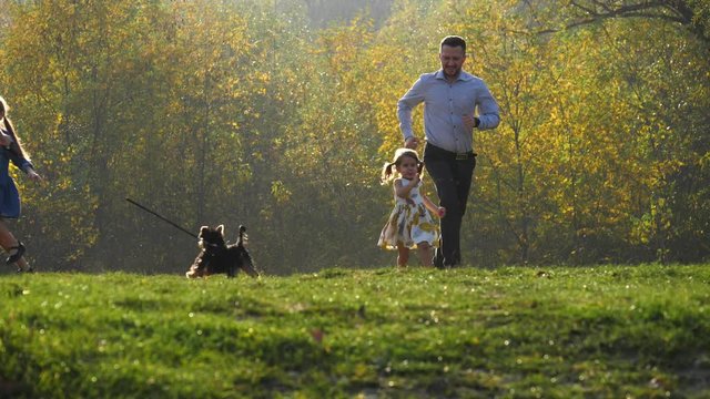 Happy young family running in the autumn park with their little dog