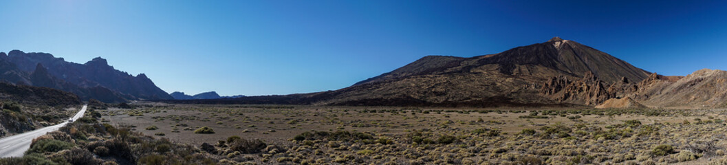 Fototapeta na wymiar Kraterebene mit Felsformation Roques de García und Vulkan Teide auf der Insel Teneriffa als Panoramabild mit Bergstraße