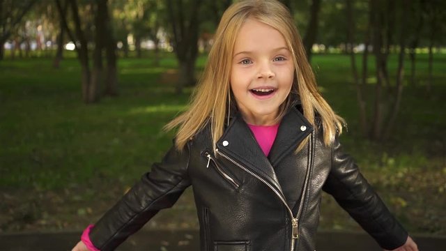 Lovely little blonde girl wearing a leather jacket is closing her eyes with her palms and opening them. Handheld real time establishing shot