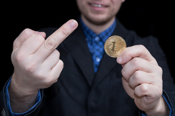 young businessman holding coin of crypto currency bitcoin and showing middle finger