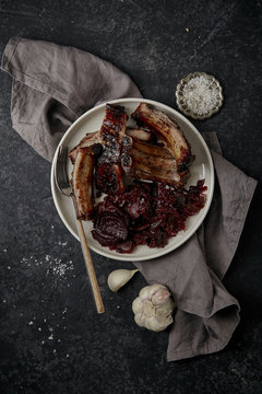 Main dish with grilled pork ribs in thick barbeque sauce garnished with red cabbage and beets braised in red wine sauce. Dark textured background
