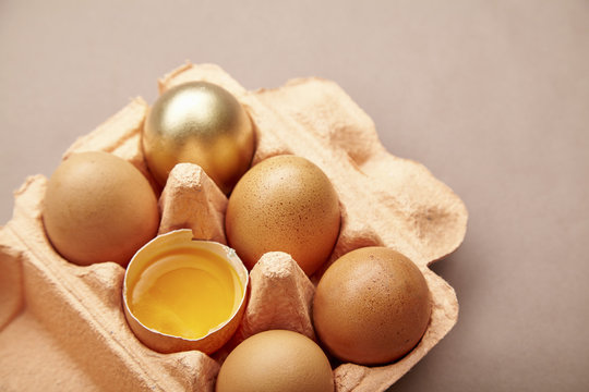 Half Dozen of chicken eggs in colorful cardboard container with one golden egg