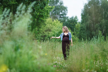 young beautiful pregnant woman is walking in the park or blossoming field